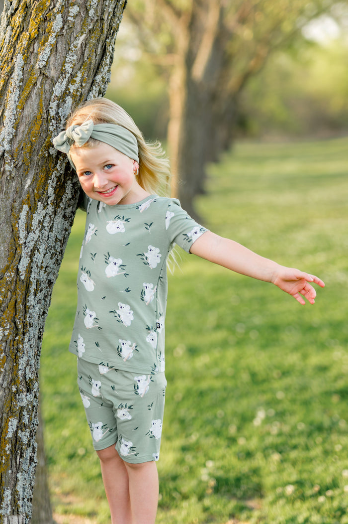 Smiling girl standing beside a tree wearing the Short Sleeve Pajamas in Koala