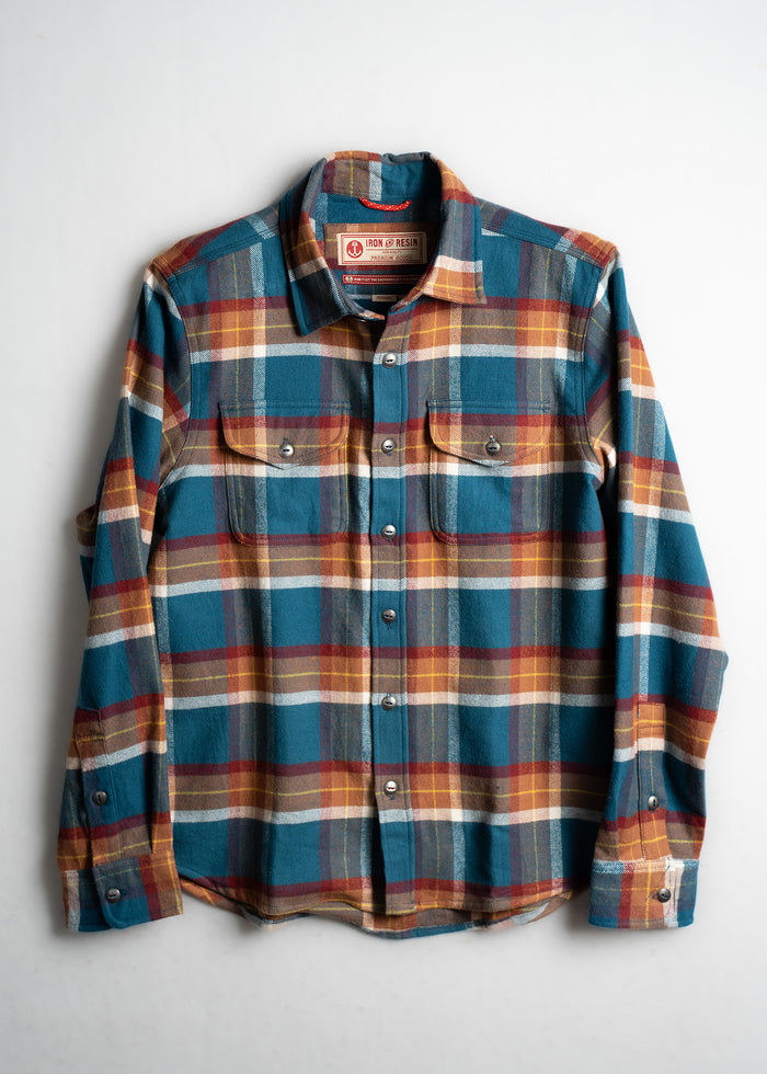 Plaid flannel shirt with blue, red, and yellow checks, featuring buttoned pockets, laid flat on a white background.