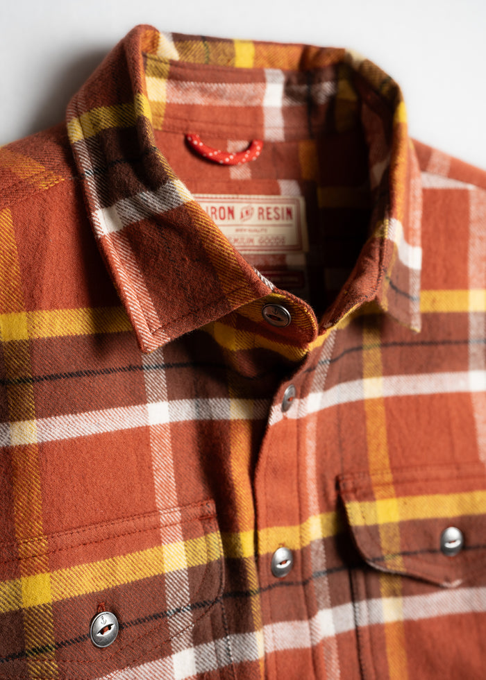 Close-up of an orange, yellow, and white plaid flannel shirt with metal buttons and a visible label inside the collar.