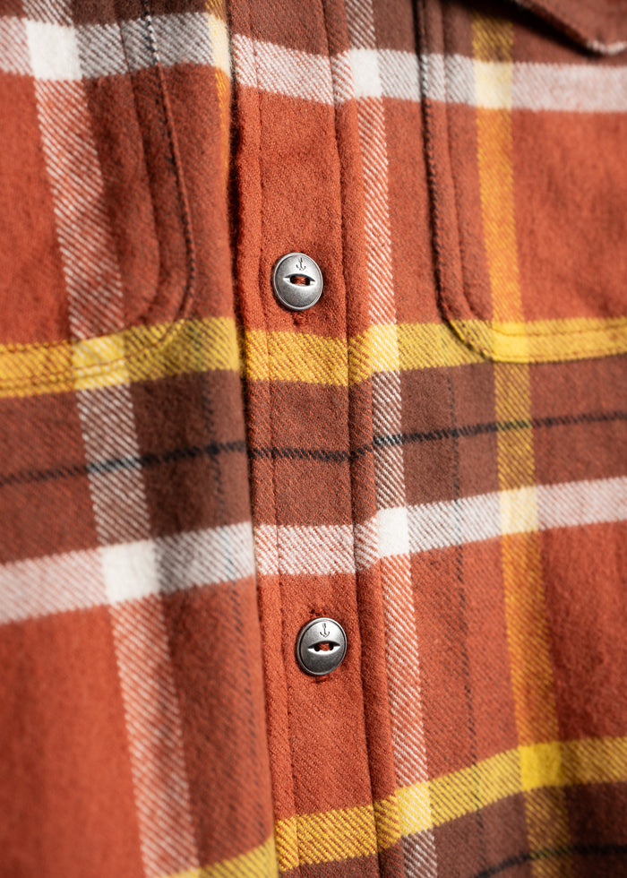 Close-up of a red, yellow, and white plaid flannel shirt with metal buttons, highlighting the fabric's texture and pattern.