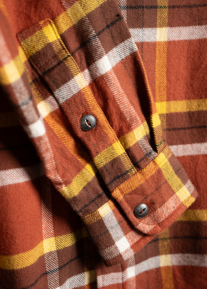 Close-up of a plaid flannel shirt in orange, brown, and yellow tones, showcasing button details and fabric texture.