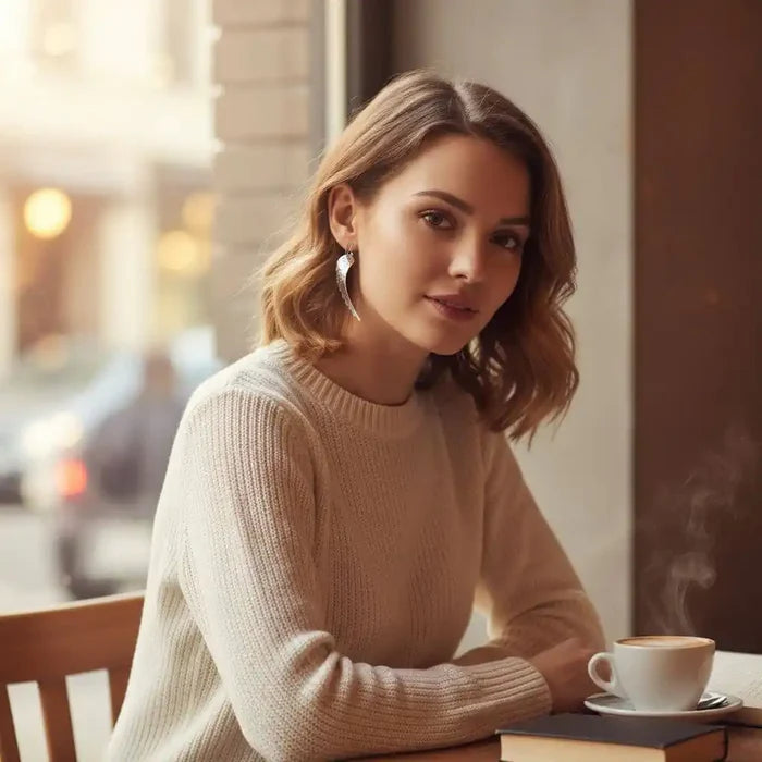 Elegant woman wearing Silver Hammered Sculpted Angel Wing Earrings while enjoying coffee at a cafe.