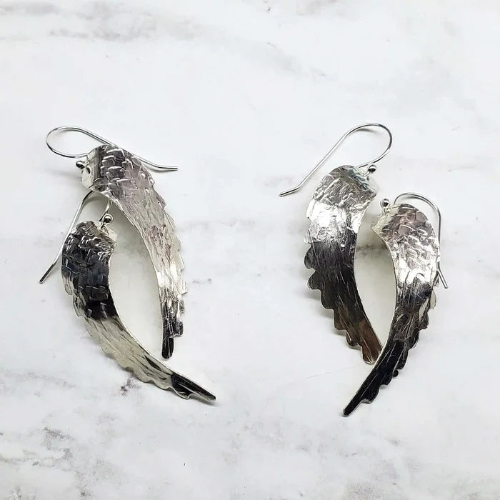 Silver Hammered Sculpted Angel Wing Earrings displayed on a marble surface, showcasing their intricate hammered texture.