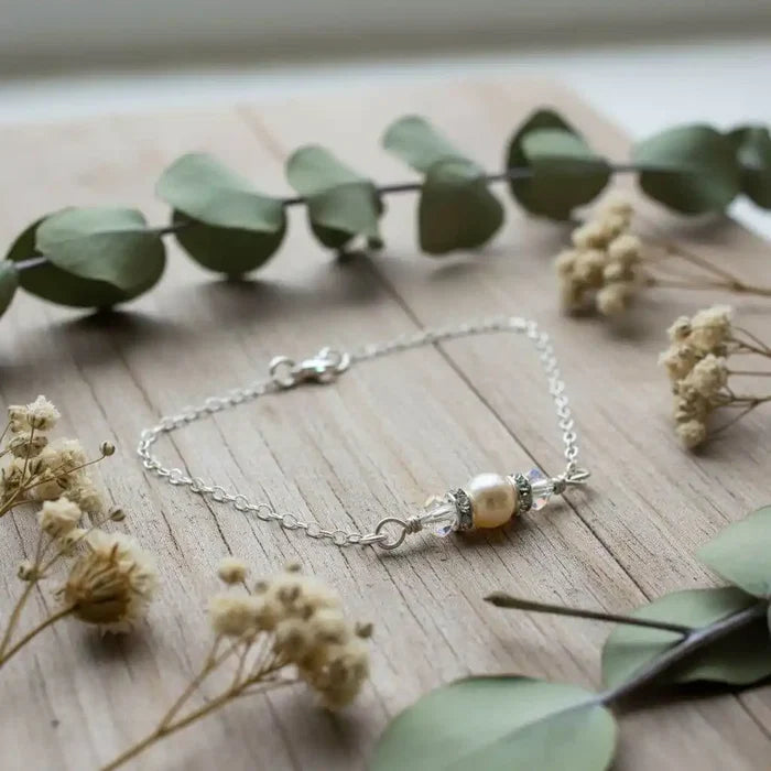Silver Swarovski Crystal Pearl Bar Bridal Bracelet on wooden surface with greenery and dried flowers.