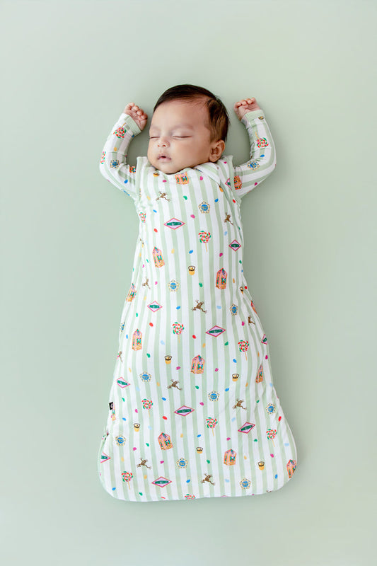 Baby asleep in a green and white striped sleep bag with colorful Harry Potter patterns on a green background