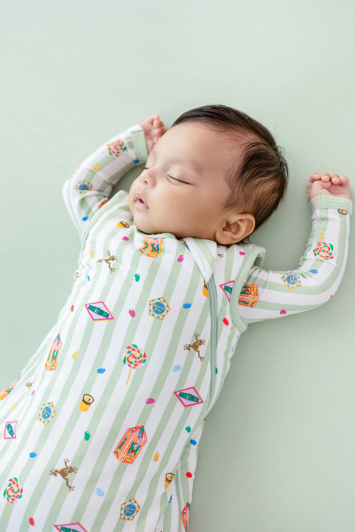 Baby sleeping in a green and white striped sleep bag with colorful Harry Potter patterns on a green background