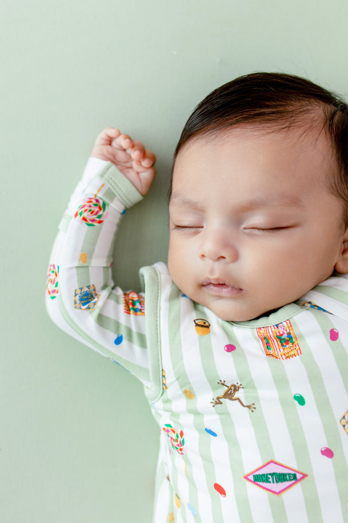 Baby sleeping in a green and white striped sleep bag with colorful Harry Potter patterns on a green background