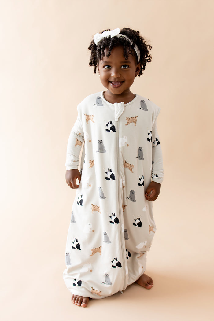 Child wearing a patterned sleep bag walker with cat designs on a beige background