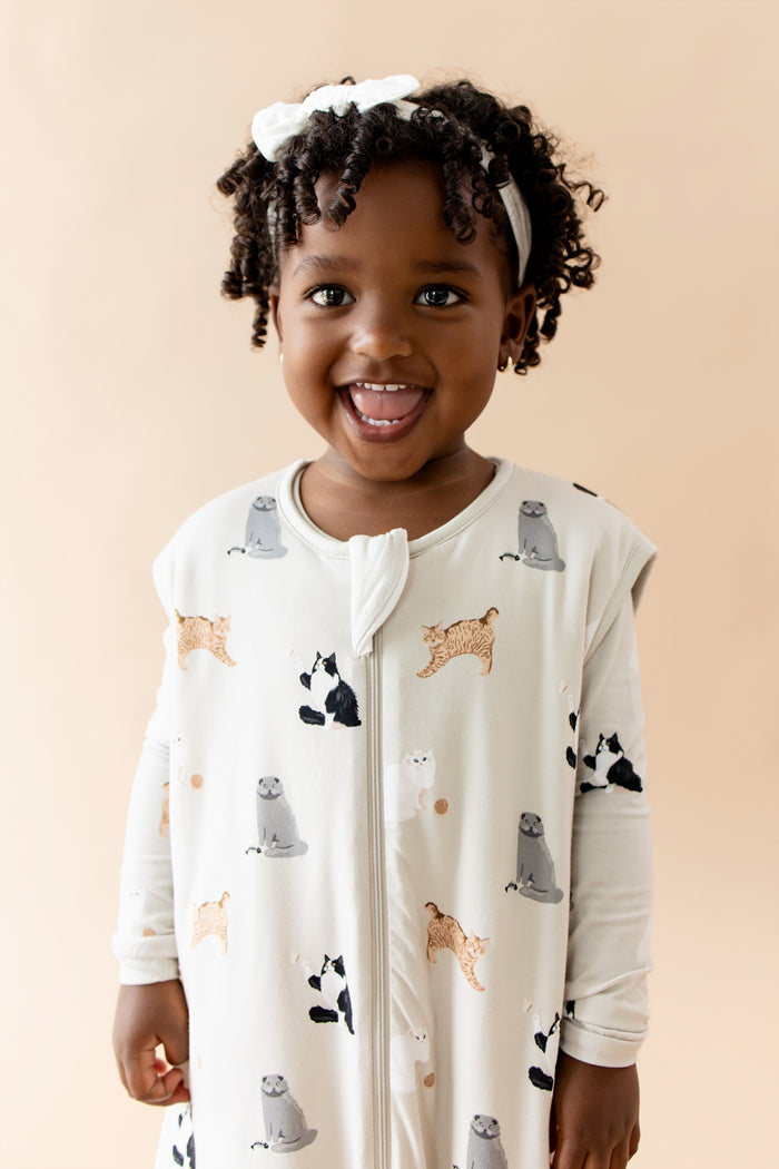 Child wearing a sleep bag walker with cat prints on a beige background