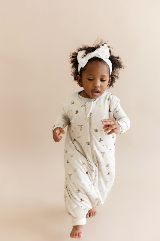 Child wearing a Harry Potter patterned sleep bag walker with white headband on a beige background