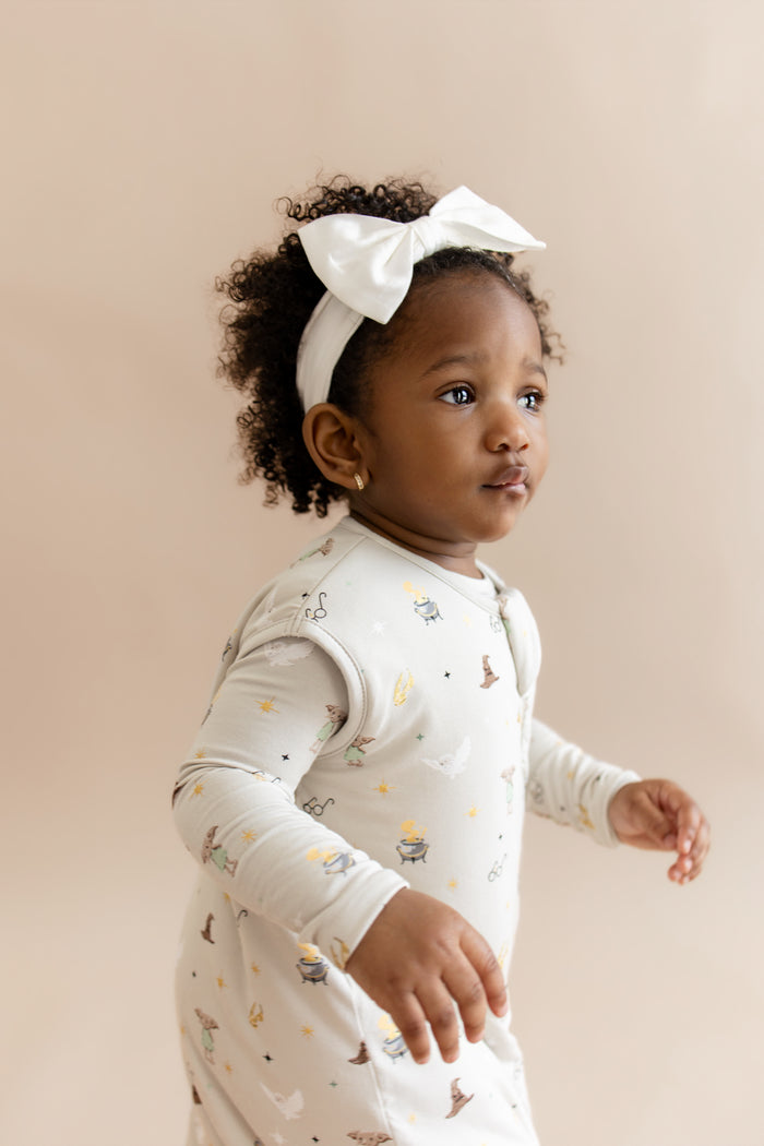 Child wearing a Harry Potter patterned sleep bag walker with a white headband on a beige background