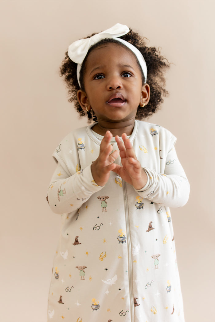 Child wearing a cream sleep bag walker with Harry Potter prints on a beige background