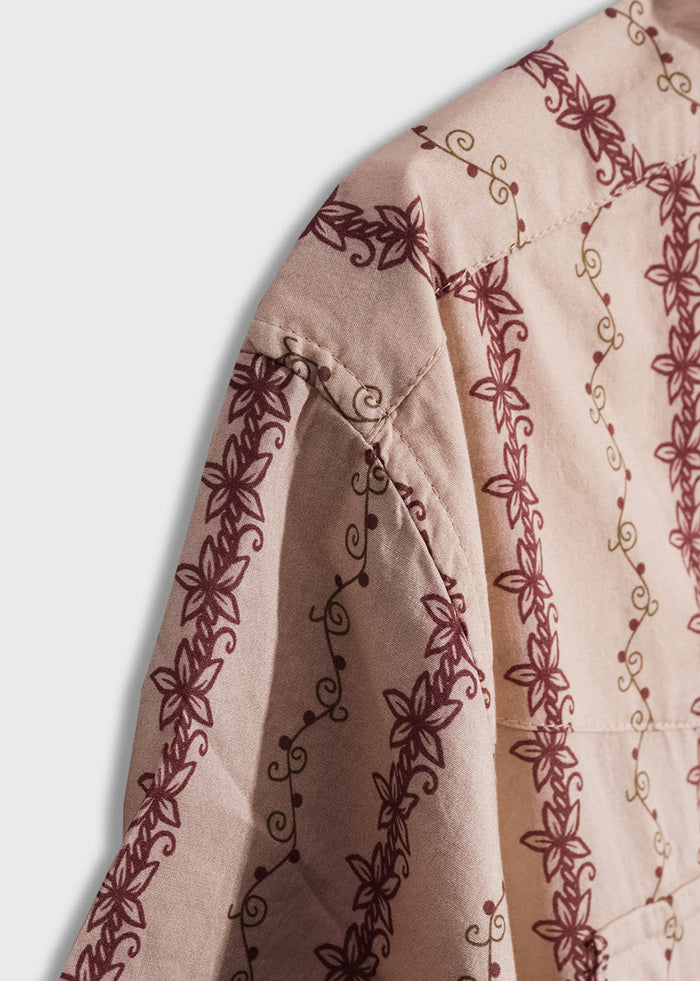 Close-up of a pink fabric with intricate maroon floral patterns and delicate swirls, highlighting detailed stitching.