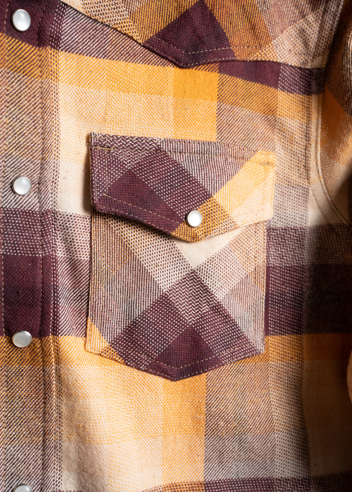 Close-up of a yellow and brown plaid shirt with a front pocket and snap buttons, highlighting the textured fabric pattern.