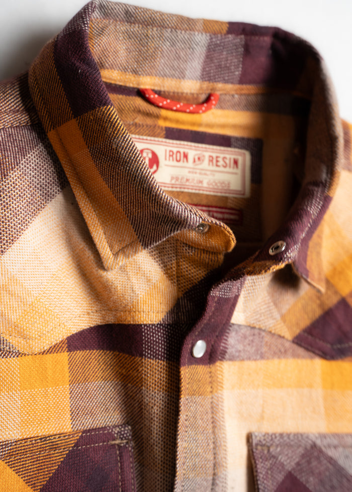 Close-up of a yellow and brown plaid shirt with a visible Iron & Resin label, highlighting its texture and button details.