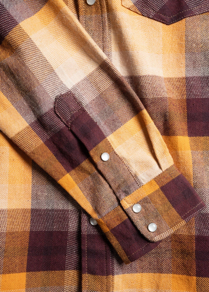 Close-up of a plaid shirt with yellow and brown checks, featuring a buttoned cuff and pocket flap, showcasing its texture.