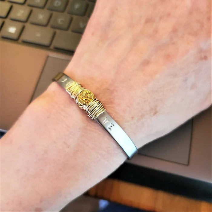 Stainless Steel LOVE Stamped Wire Wrapped Gold Druzy Cuff worn on wrist near laptop.
