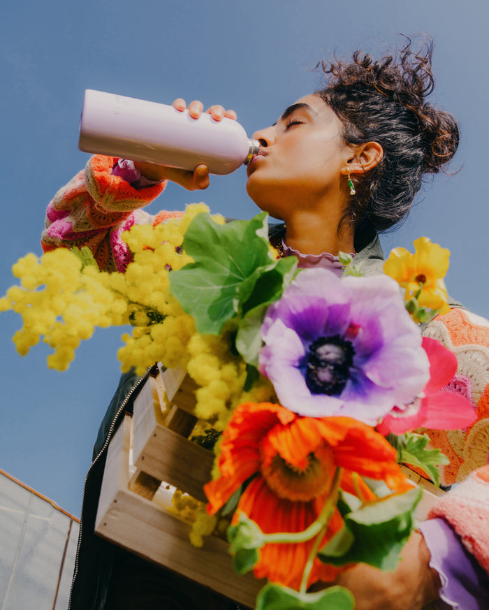 Woman drinking from a pastel glossy stainless steel bottle, showcasing the product’s sleek design and limited edition availability.