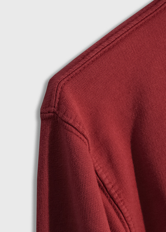Close-up of a red sweatshirt's shoulder seam, showcasing detailed stitching and texture against a light gray background.