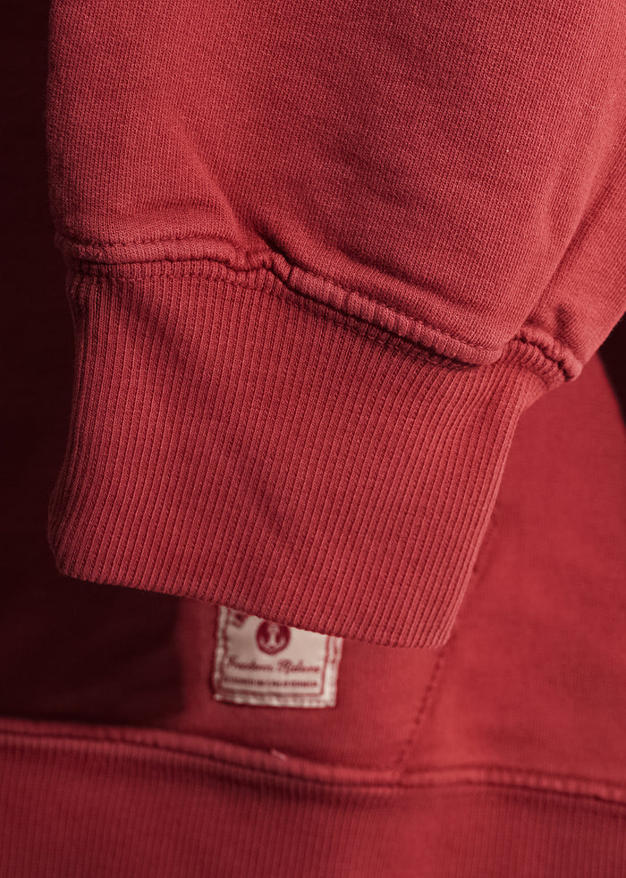 Close-up of a red sweatshirt sleeve with ribbed cuff, showcasing a small label with text, highlighting garment details.