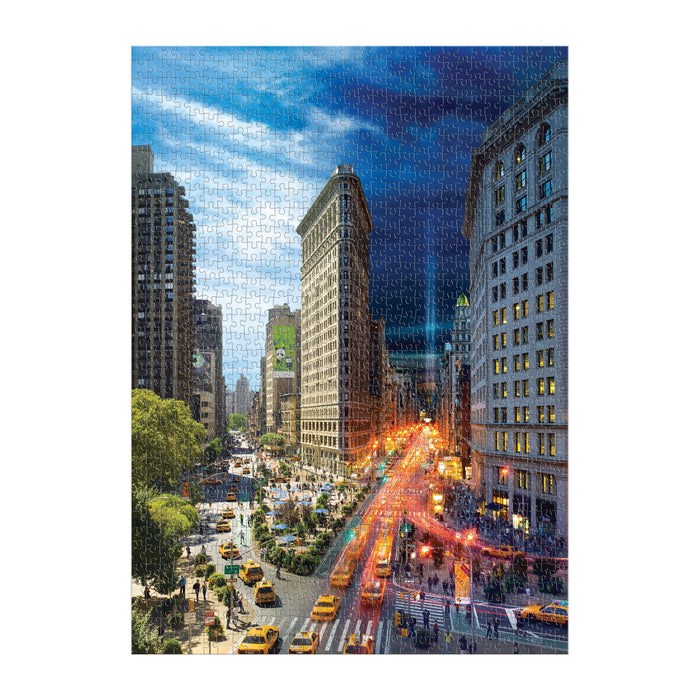 The Stephen Wilkes Day To Night Flatiron 1000 Piece Puzzle by Stephen Wilkes features a New York Cityscape with tall buildings, yellow taxis, busy streets, and the iconic Flatiron Building transitioning from day to night.
