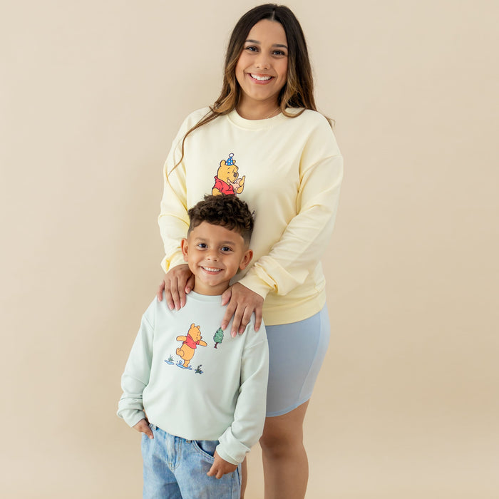 Son wearing the Sweatshirt in Winnie the Pooh on Dew standing in front of his mother who is wearing the matching women's sweater in Winnie the Pooh on Chamomile
