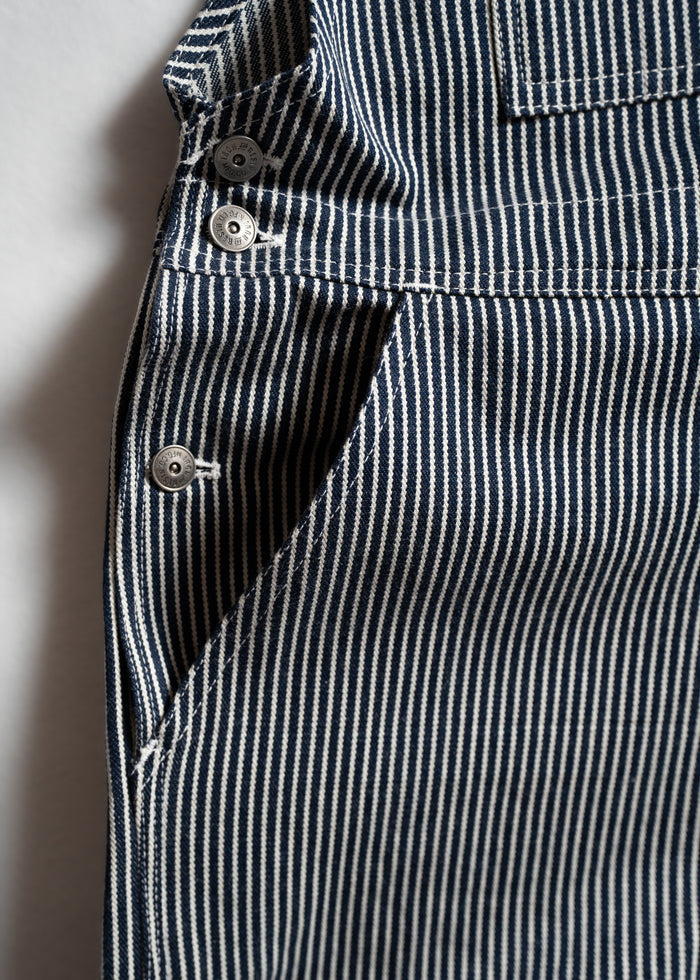 Close-up of blue and white striped fabric with metal buttons, showcasing detailed stitching and texture in natural light.