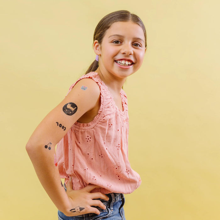 Girl with several Tattoo-Palooza x Suzy Ultman: Temporary Tattoos on yellow background