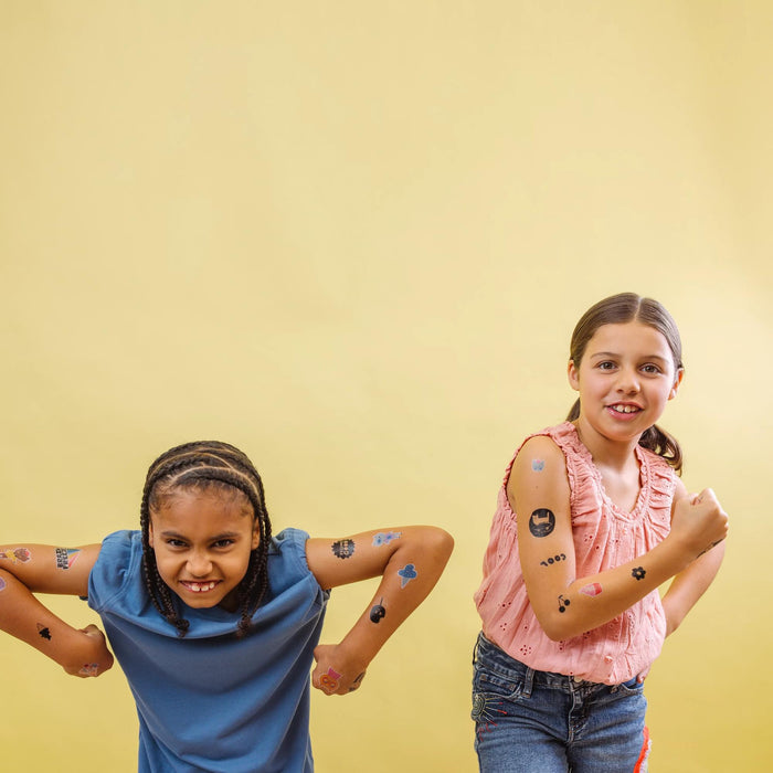 Two girls posting with Tattoo-Palooza x Suzy Ultman: Temporary Tattoos on yellow background