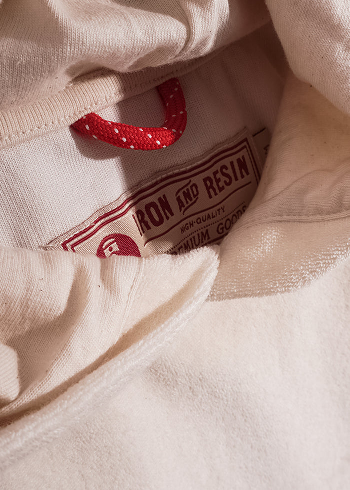 Close-up of a cream hoodie with a red drawstring and "Iron and Resin" label, highlighting its high-quality, premium design.