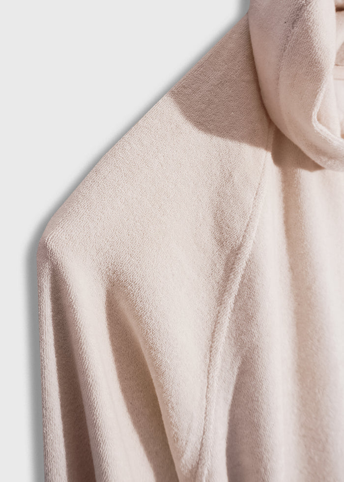 Close-up of a beige textured hoodie, showcasing its soft fabric and subtle shadowing, highlighting the garment's cozy appeal.