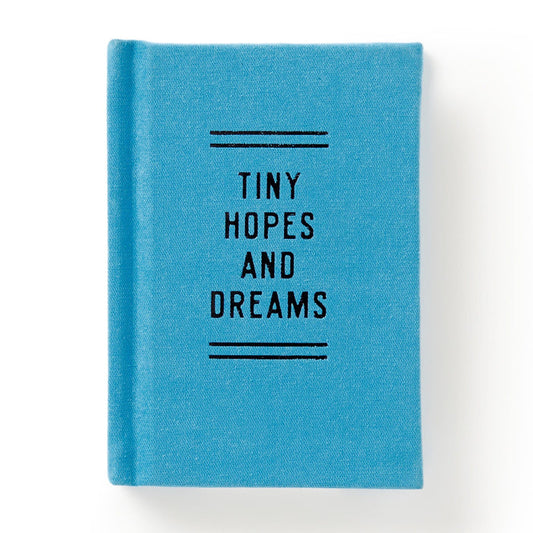 The Brass Monkey Tiny Hopes and Dreams Tiny Diary is a small, blue hardbound notebook with Tiny Hopes and Dreams in black on the cover, along with decorative lines. Photographed against a white background.