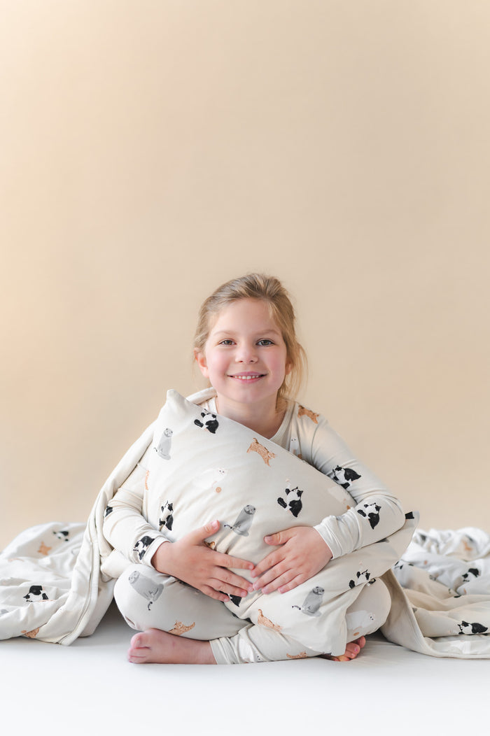 Child wrapped in a soft blanket with cat patterns and holding a matching pillow on a plain background