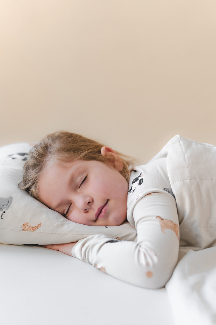 Child sleeping on a cat printed pillow with a neutral background