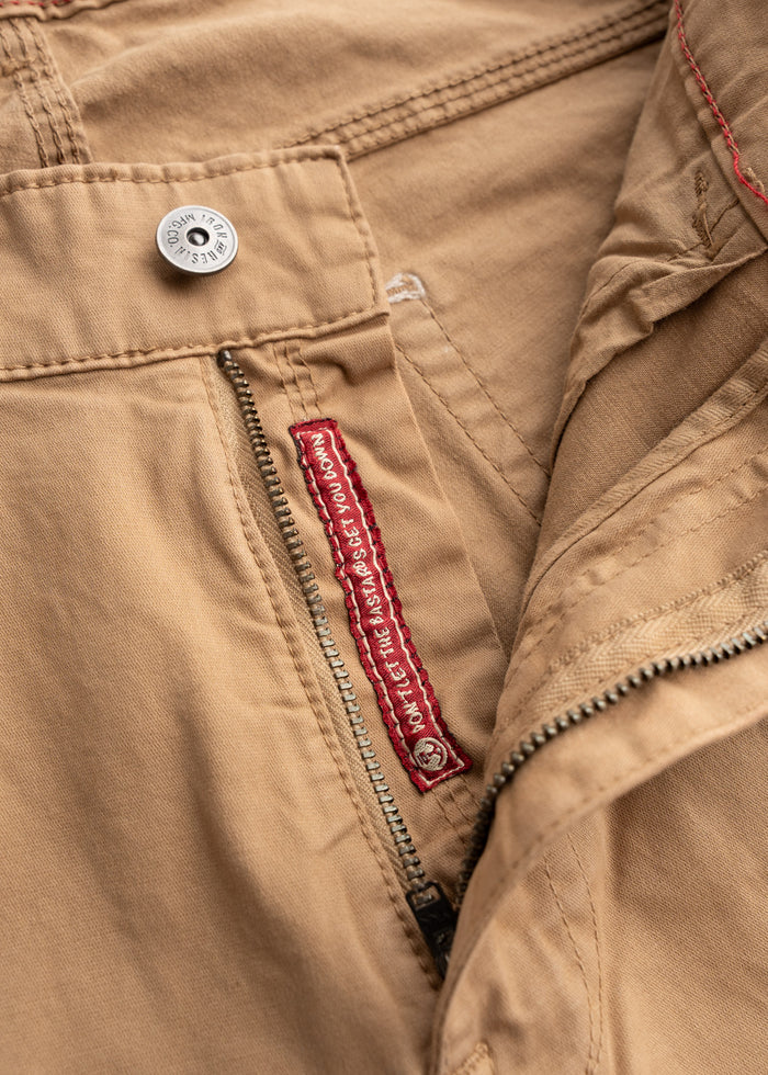 Close-up of khaki pants with a metal button and zipper. Red label inside reads, "Don't let the bastards grind you down."