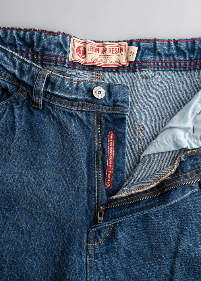 Close-up of blue jeans with Iron and Resin label, size 32. Visible zipper and button detail on light gray background.