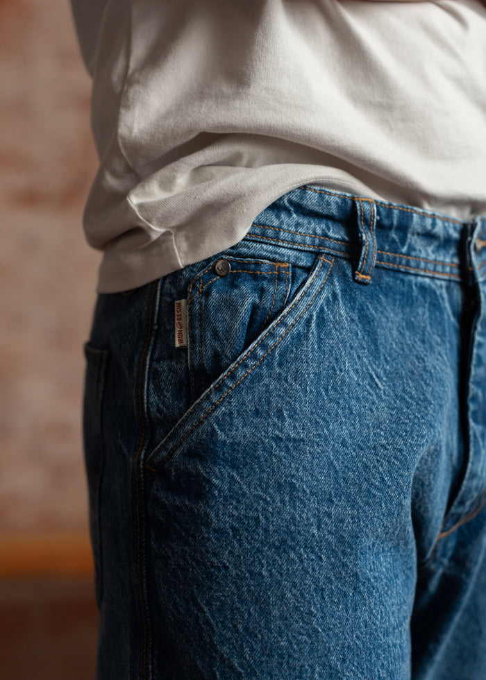 Close-up of a person in a white shirt and blue jeans, showing the denim texture and casual style against a blurred background.