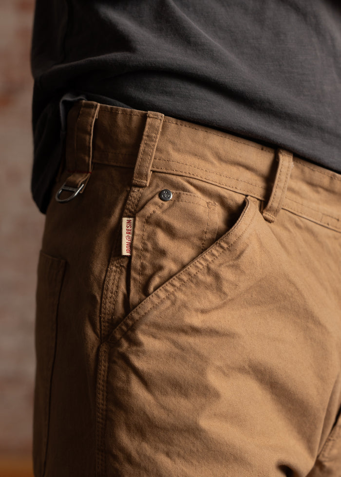 Close-up of a person wearing brown pants with a visible brand tag, paired with a dark shirt, highlighting casual style.