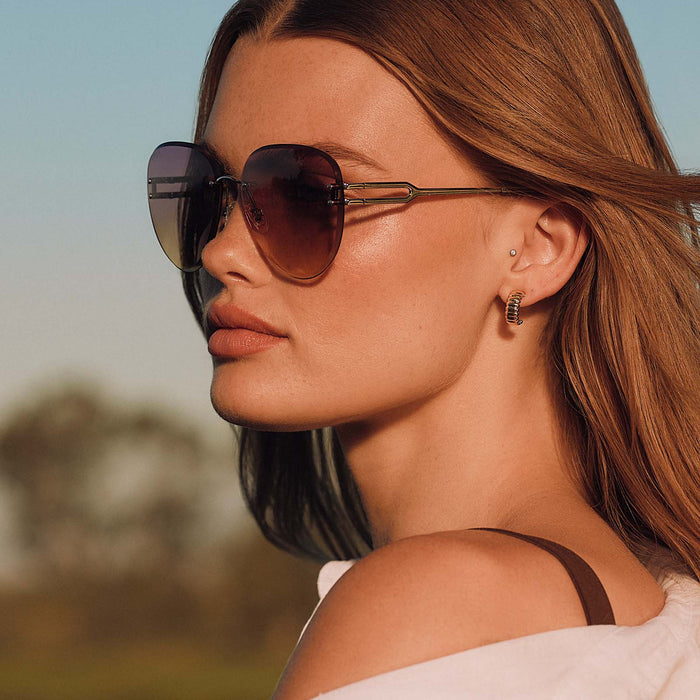 lifestyle - female outdoors wearing diff eyewear featuring the trista aviator sunglasses with a gold frame and misty lilac gradient lenses side view