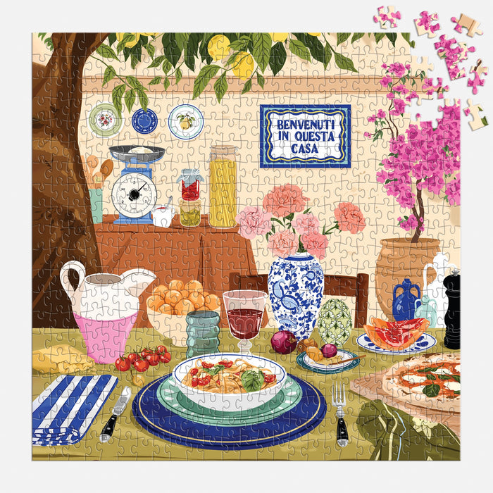 The Ana Hard Tuscan Afternoon 500 Piece Puzzle captures an outdoor Italian table scene with food, drinks, and flowers, plus a Benvenuti in questa casa sign, with some pieces unplaced to complete the charming look.