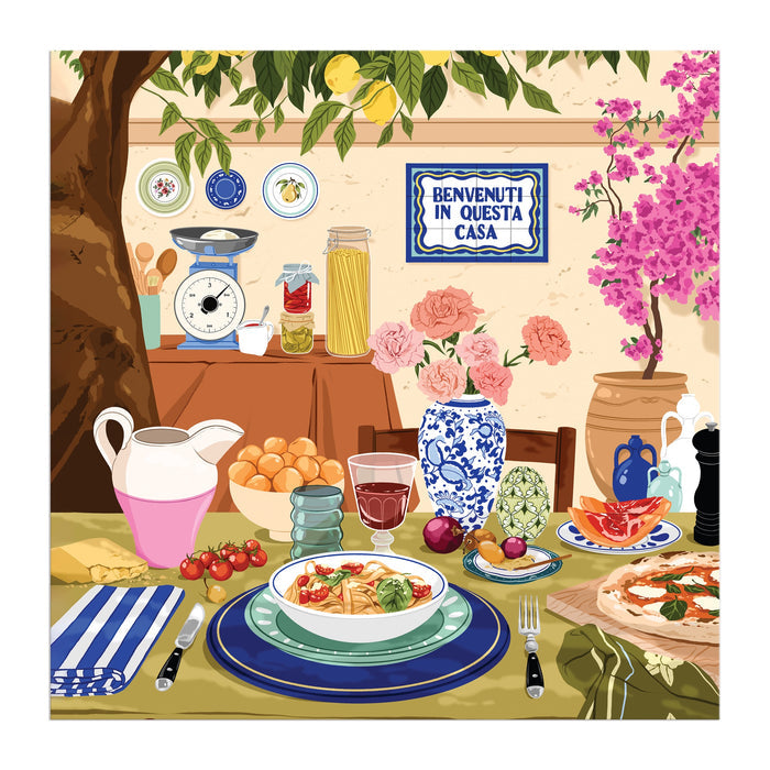 The Ana Hard Tuscan Afternoon 500 Piece Puzzle features a vibrant Italian outdoor table set with pasta, bread, fruit, drinks, decorative plates, and a Benvenuti in Questa Casa sign, all framed by trees and bright flowers.