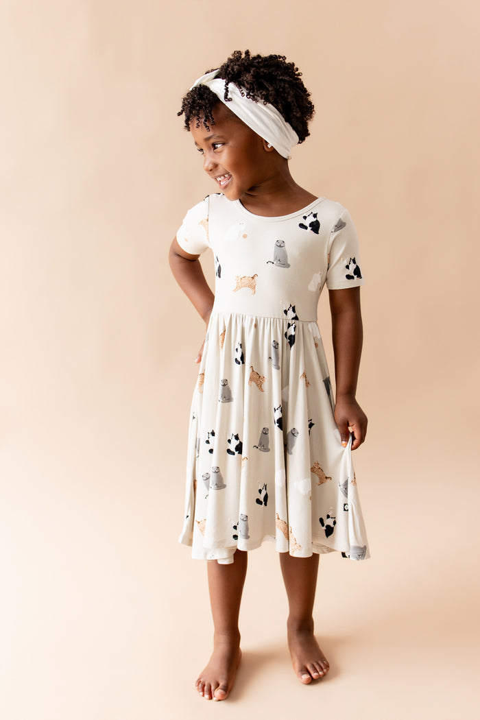 Young smiling girl posing wearing the Twirl Dress in Fluffy Cat with white bow