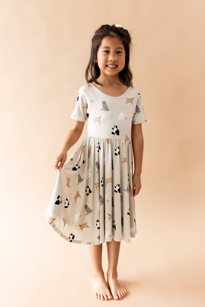Young girl smiling wearing the Twirl Dress in Fluffy Cat holding the skirt of the dress