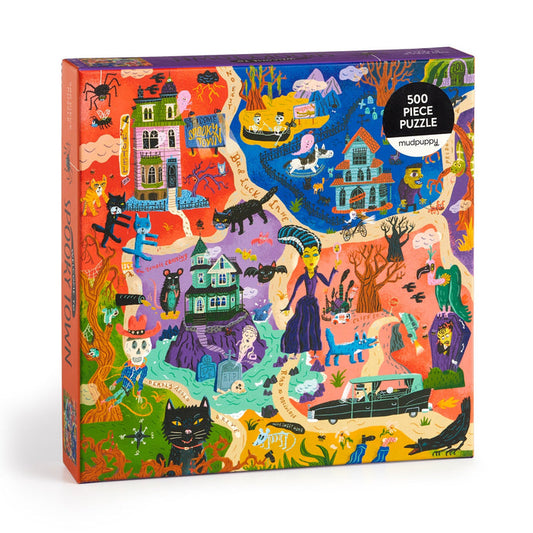 The Welcome to Spooky Town 500 Piece Puzzle by Stephanie Birdsong features a vibrant haunted town scene with ghosts, skeletons, witches, a black cat, vampire, hearse, bats, and pumpkins scattered throughout.