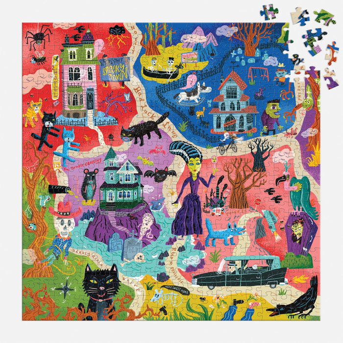 The Stephanie Birdsong Welcome to Spooky Town 500 Piece Puzzle features vibrant haunted houses, black cats, ghosts, skeletons, a vampire, bats, a hearse, and monsters—plus some unplaced pieces in the top right corner.