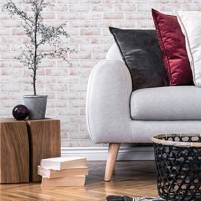 Tempaper's Whitewashed Brick Peel And Stick Wallpaper behind a plant and a grey couch with pillows. #color_whitewashed