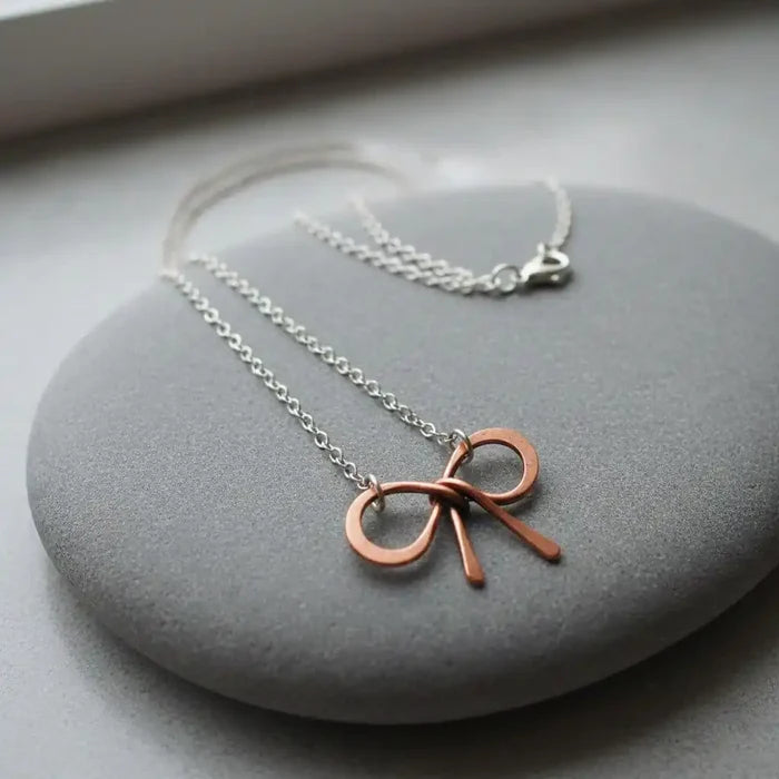 Wire Wrapped Copper Bow Tie Silver Chain Necklace on smooth grey stone background.