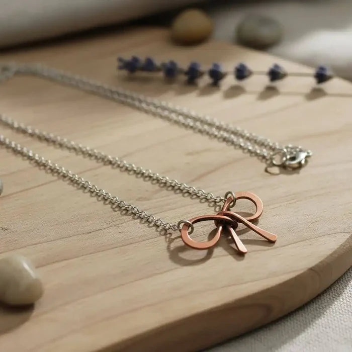 Wire Wrapped Copper Bow Tie Silver Chain Necklace on a wooden surface with stones and lavender.