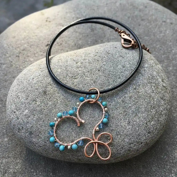 Wire Wrapped Copper Turquoise Heart Infinity Charm Necklace on a stone background