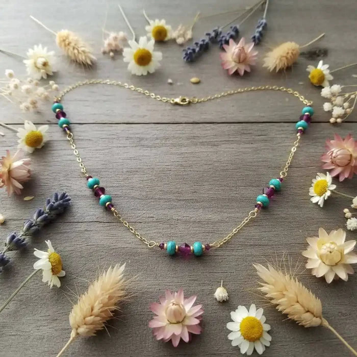 Wire Wrapped Gold Filled Pink Turquoise Gemstone Necklace with heishi beads and Swarovski crystals, surrounded by flowers.
